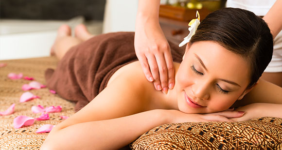 a woman with flower petals adorned around her smiling as she receives a shoulder massage