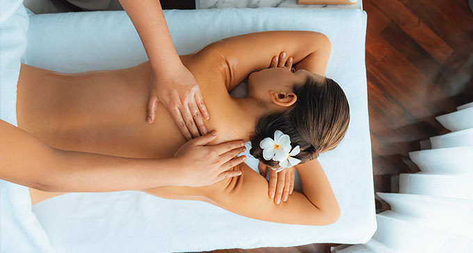 a woman receiving a body pampering to her back with flowers in her hair