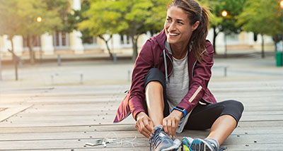 a woman fastening her running shoes on a decking with her phone and earphones on the ground next to her