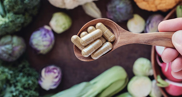 a wooden spoon of supplements above a surface of different vegetables