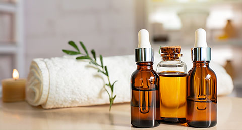 three bottles of oils used for massages with a white towel and sprig in the background