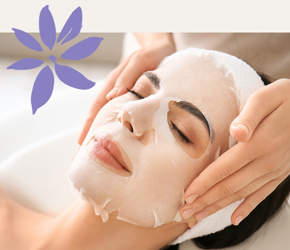 a woman receiving a face mask onto her face from a beautician